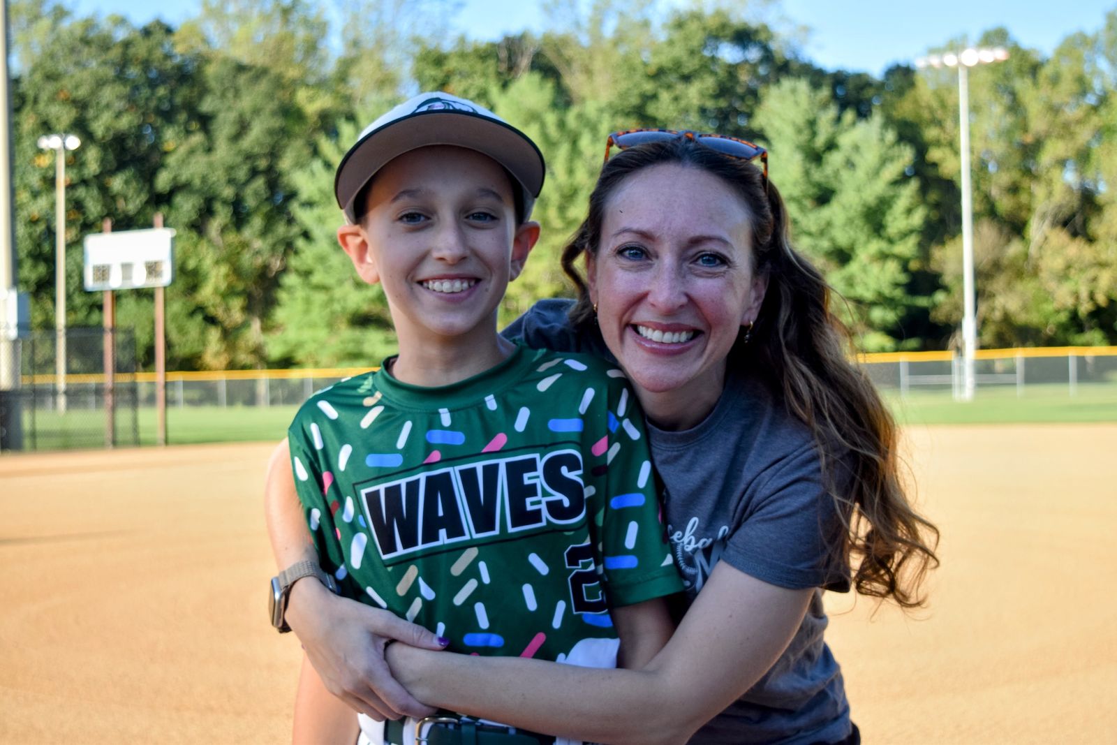 Naomi and her son Eli smiling together on a baseball field, Eli in his Waves jersey